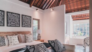 A bedroom with a large bed, multiple pillows, a nightstand, a lamp, and framed artwork on the wall. - Relax & rejuvinate at Muda Living, only minutes from Ubud Market! (Ubud)