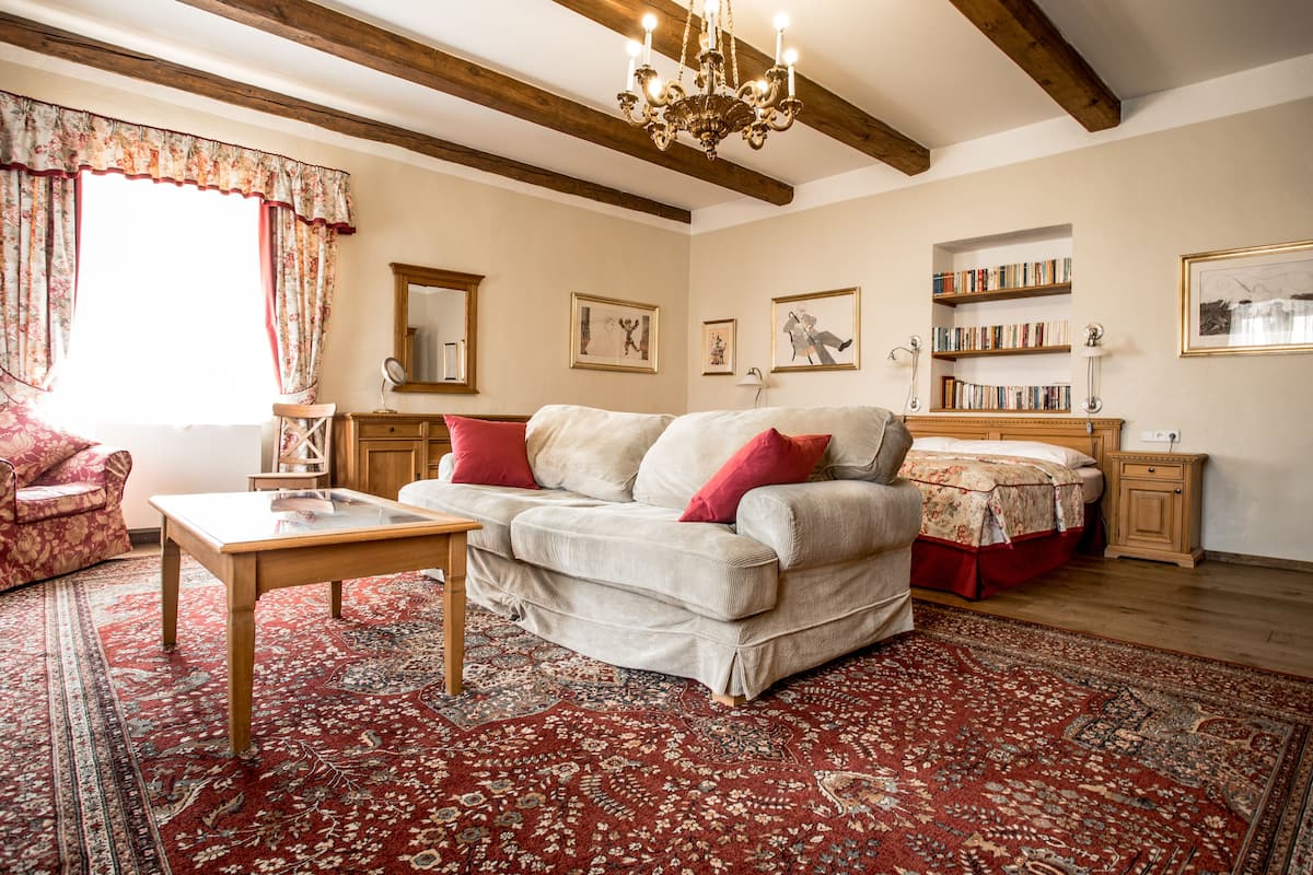 A cozy living room with a sofa, a wooden coffee table, and a red patterned rug. There are bookshelves and a chandelier.