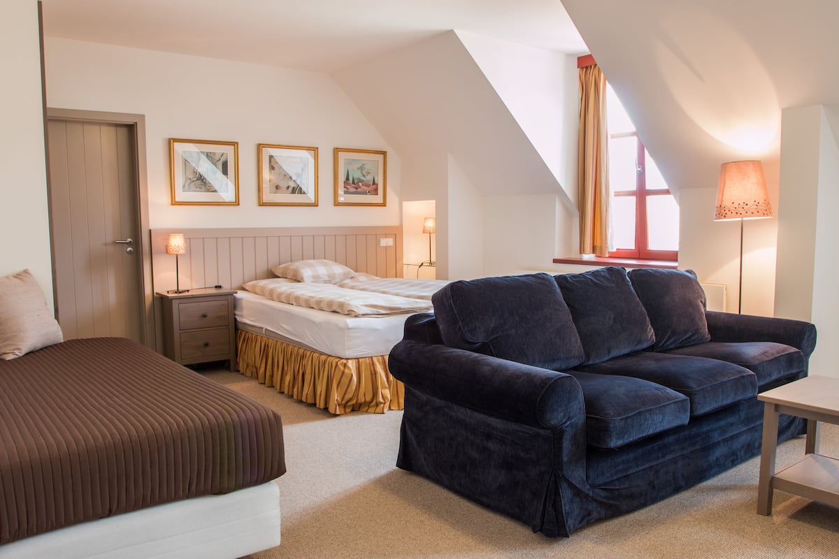 A bedroom with a bed, a sofa, a nightstand, a lamp, and a window with curtains.