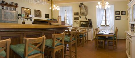 A dining area with wooden chairs and tables, a bar counter, and various wall decorations including framed pictures and a horse sculpture.