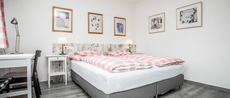 Un dormitorio con una cama, un escritorio y una silla. Hay cuatro cuadros en la pared.