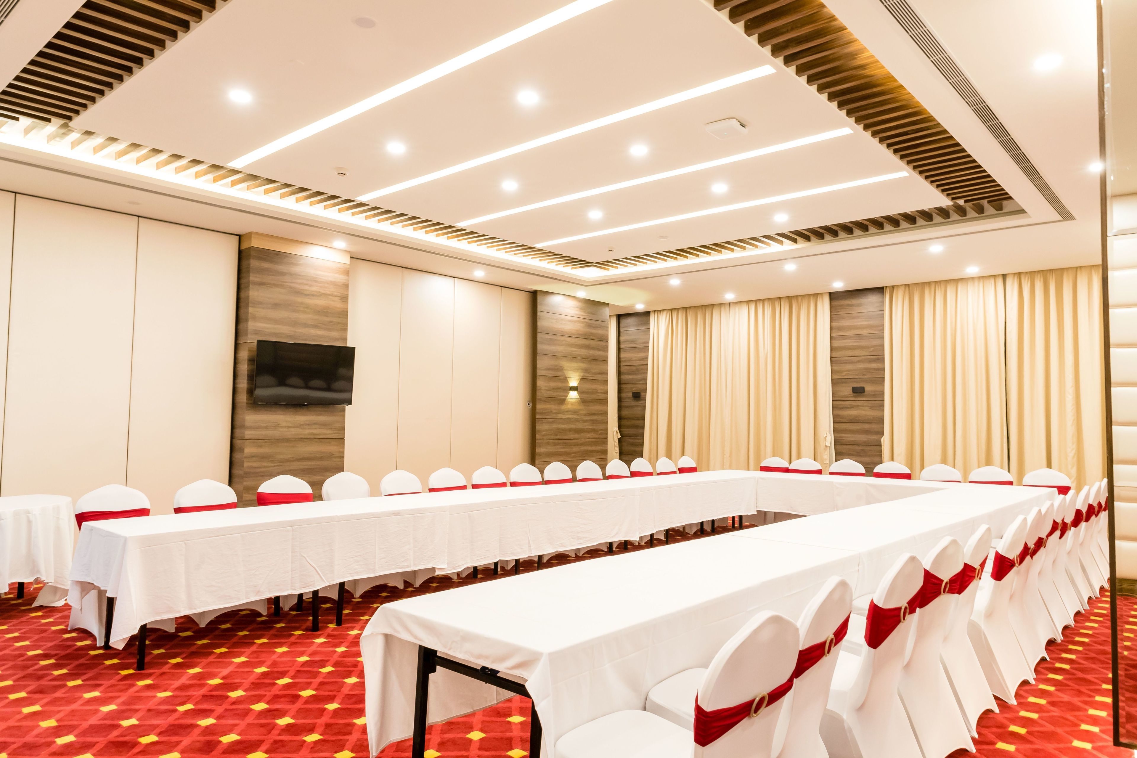 A conference room with a long table, white chairs with red sashes, and a red carpeted floor.