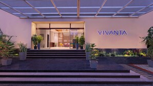 Fachada de hotel de vidrio, con escalones que conducen a la entrada y un letrero que dice "VIVANTA".