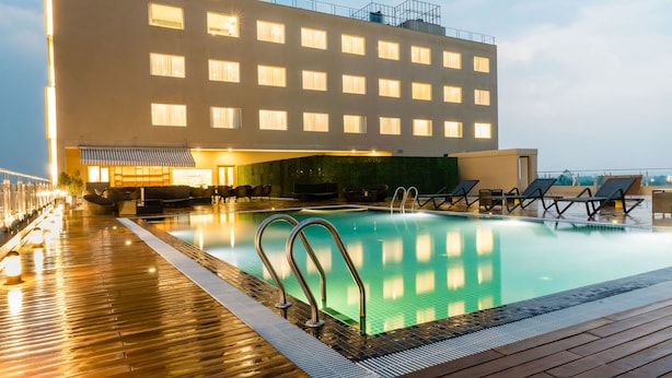 Un área de piscina en la azotea con cubierta de madera, sillas de descanso y un edificio con múltiples ventanas.
