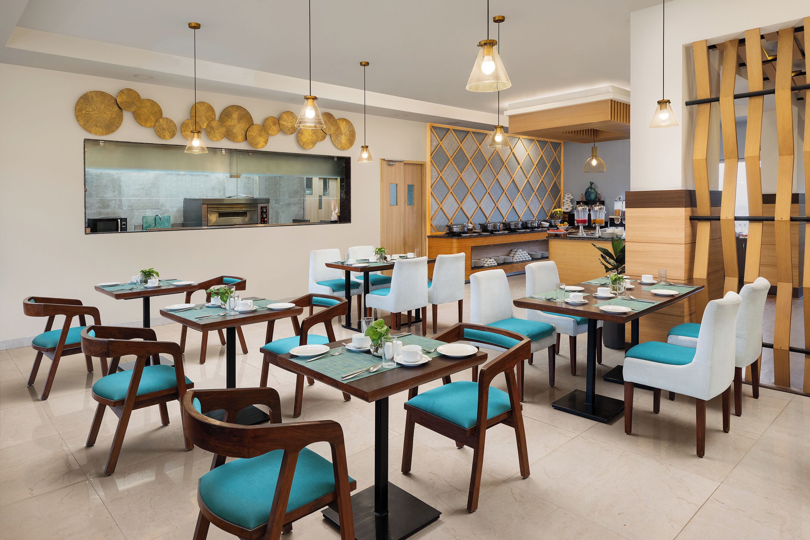 A restaurant with wooden tables and chairs, a kitchen in the background, and hanging pendant lights.