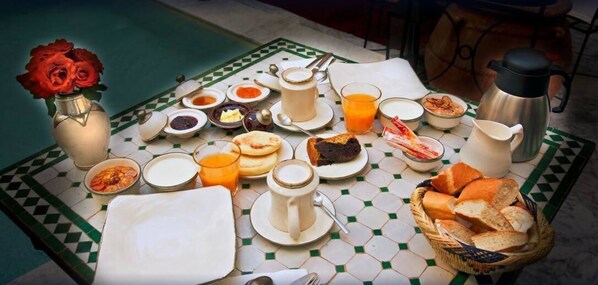 Une table de petit-déjeuner avec divers aliments, un thermos et un vase rempli de roses.