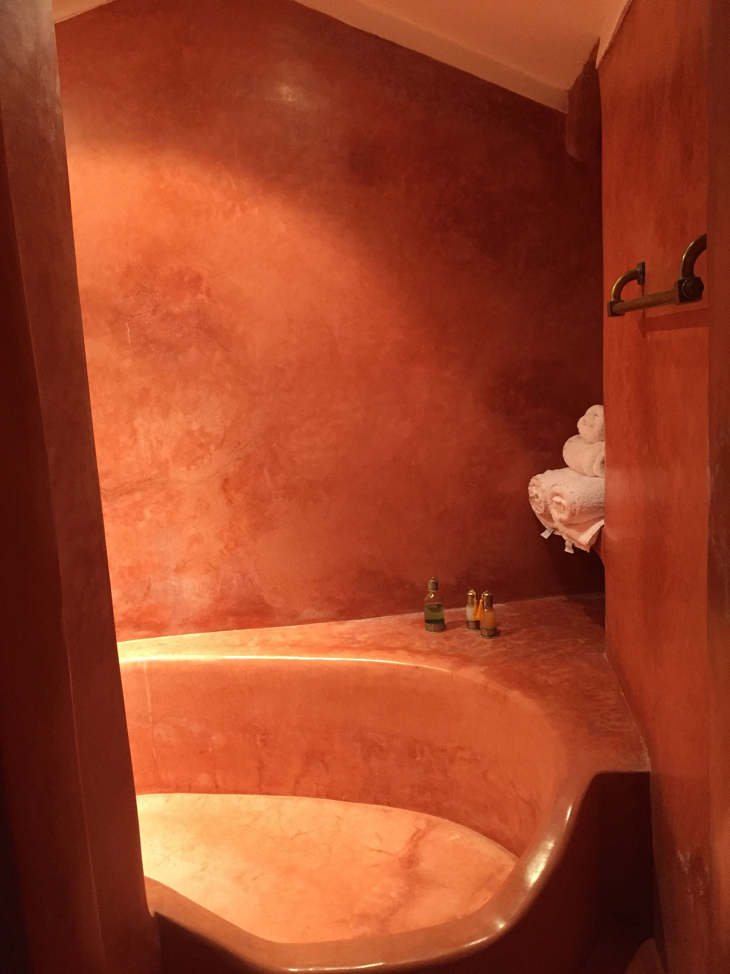 Casa de banho com uma banheira grande e curva, um porta-toalhas com toalhas dobradas e uma prateleira com produtos de higiene pessoal.