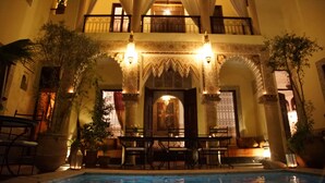 A pool area with a dining setup, surrounded by ornate architecture and potted plants. - Riad Al Loune (Marrakech)