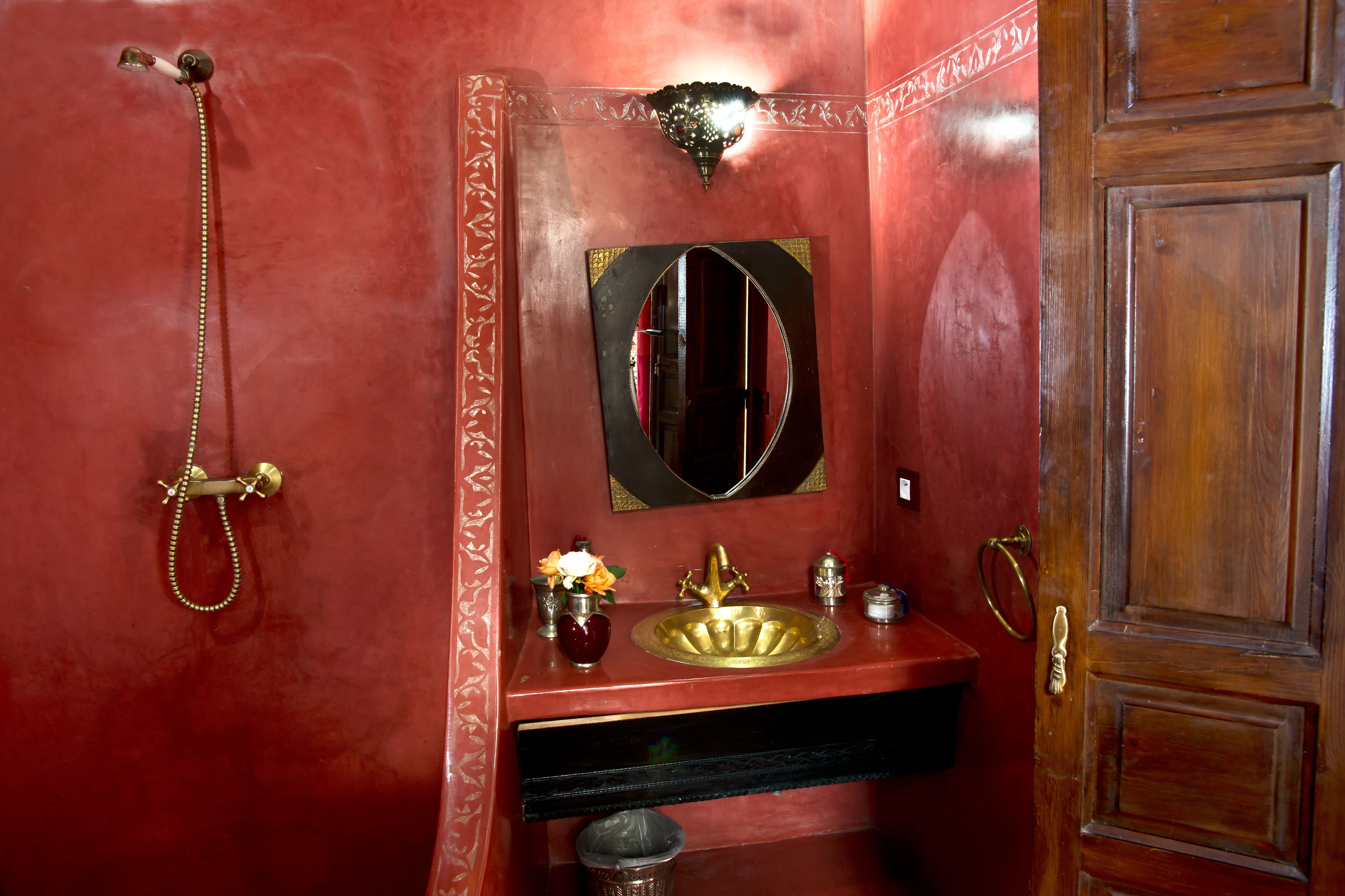 Un baño con pared roja, lavamanos dorado, espejo y ducha.