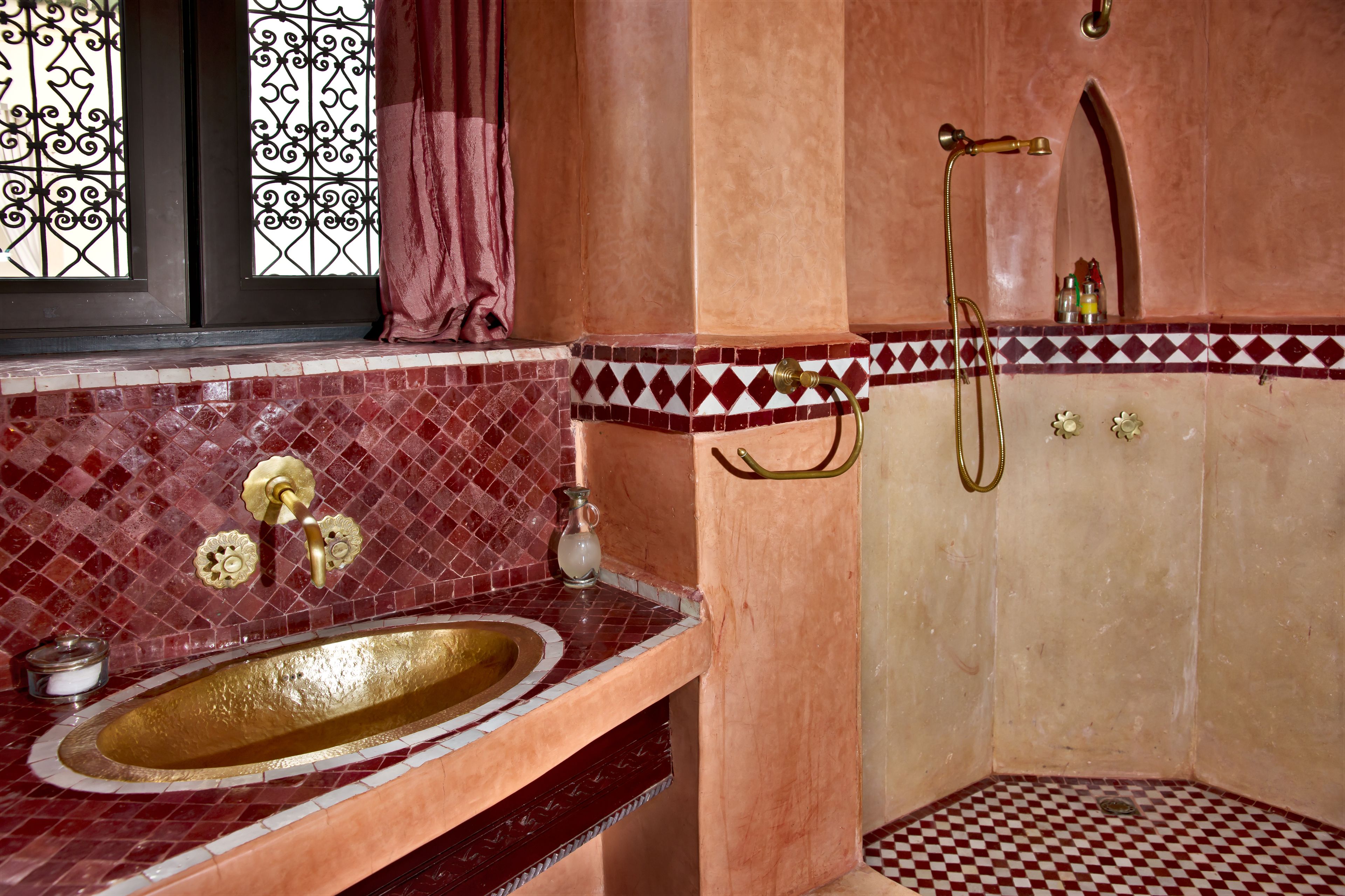 A bathroom with a gold sink, a shower, and a tiled wall with a geometric pattern.