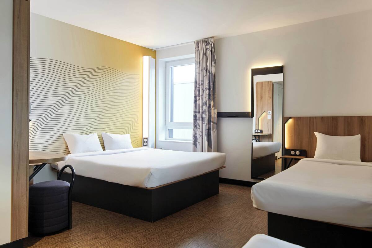Ein Hotelzimmer mit zwei Betten, einem großen Fenster mit Vorhängen, Holzboden und modernem Wanddesign.