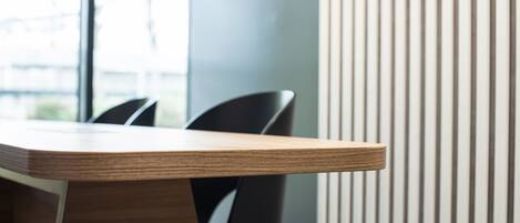 Una mesa de conferencia moderna con sillas, ubicada cerca de una ventana con persianas verticales.