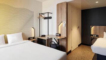 Quarto de hotel com uma cama grande, uma escrivaninha com cadeira, um cabideiro e um guarda-roupa.