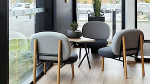 Un área de estar moderna en el interior, con dos sillas grises, una mesita y una planta en maceta.