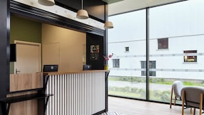 Un mostrador de recepción moderno con una computadora portátil, una planta en maceta y vistas al exterior.