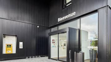 Un edificio moderno con un cartel de 'Bienvenue', puertas de cristal y un pequeño espacio al aire libre con mesas y sillas.
