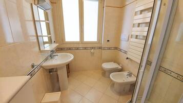 A bathroom with a sink, toilet, bidet, and a shower stall.