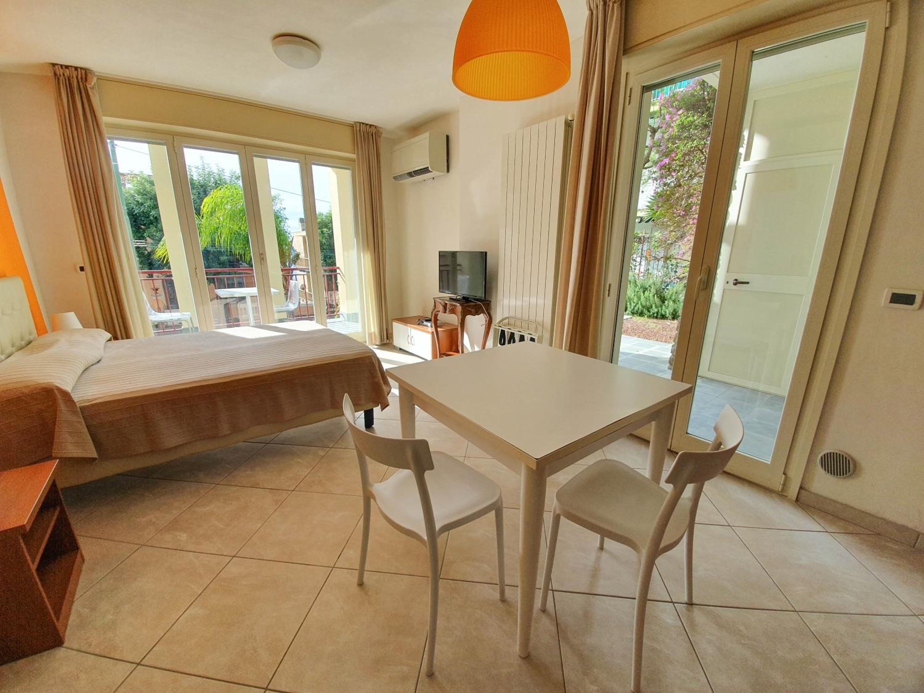 A hotel room with a bed, a dining table with chairs, a TV, and a sliding glass door to the outside.