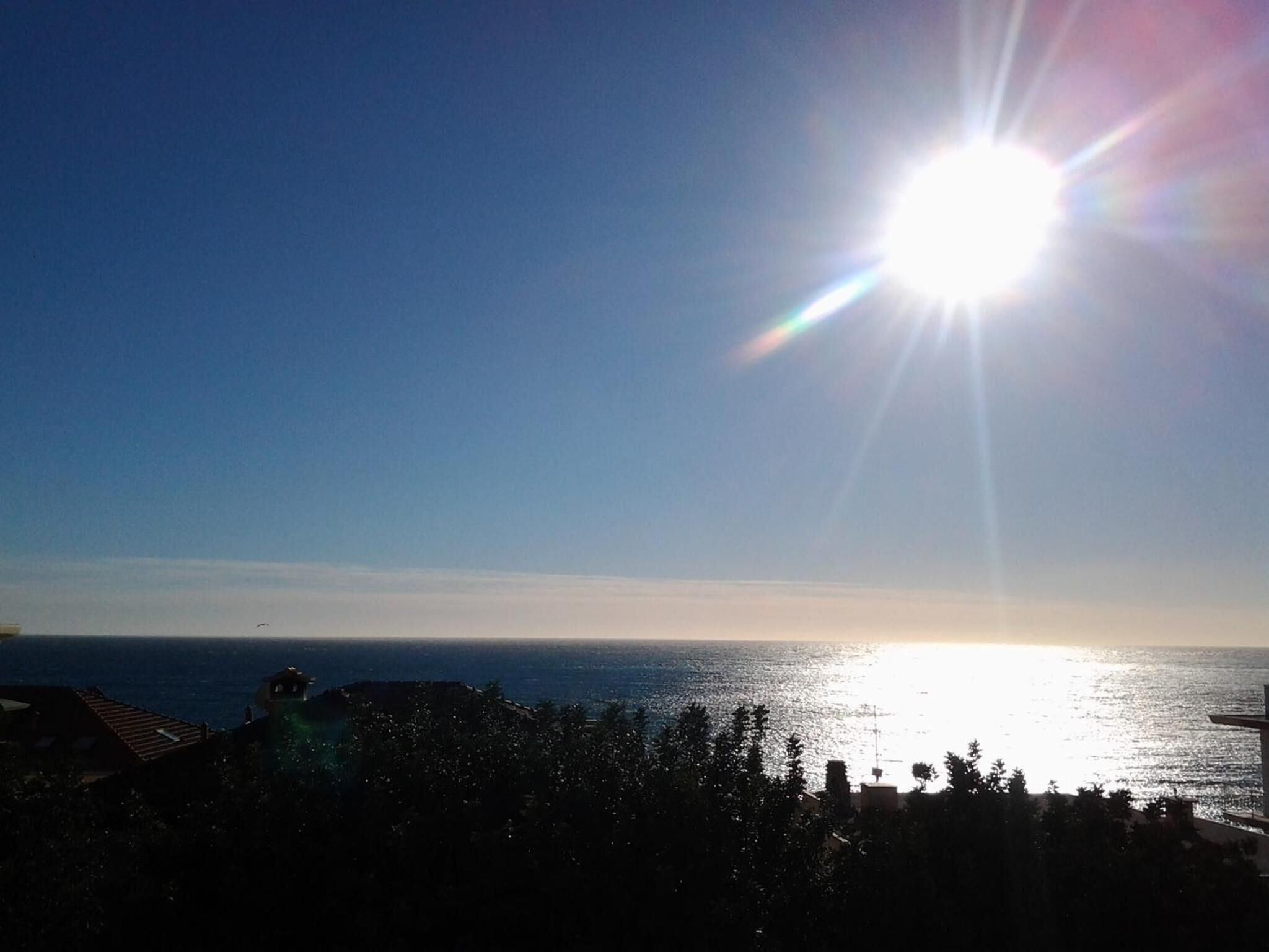 A clear view of the ocean with the sun low on the horizon, creating a lens flare effect.