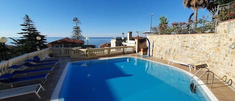 A swimming pool with lounge chairs, a stone wall, and a view of the sea.