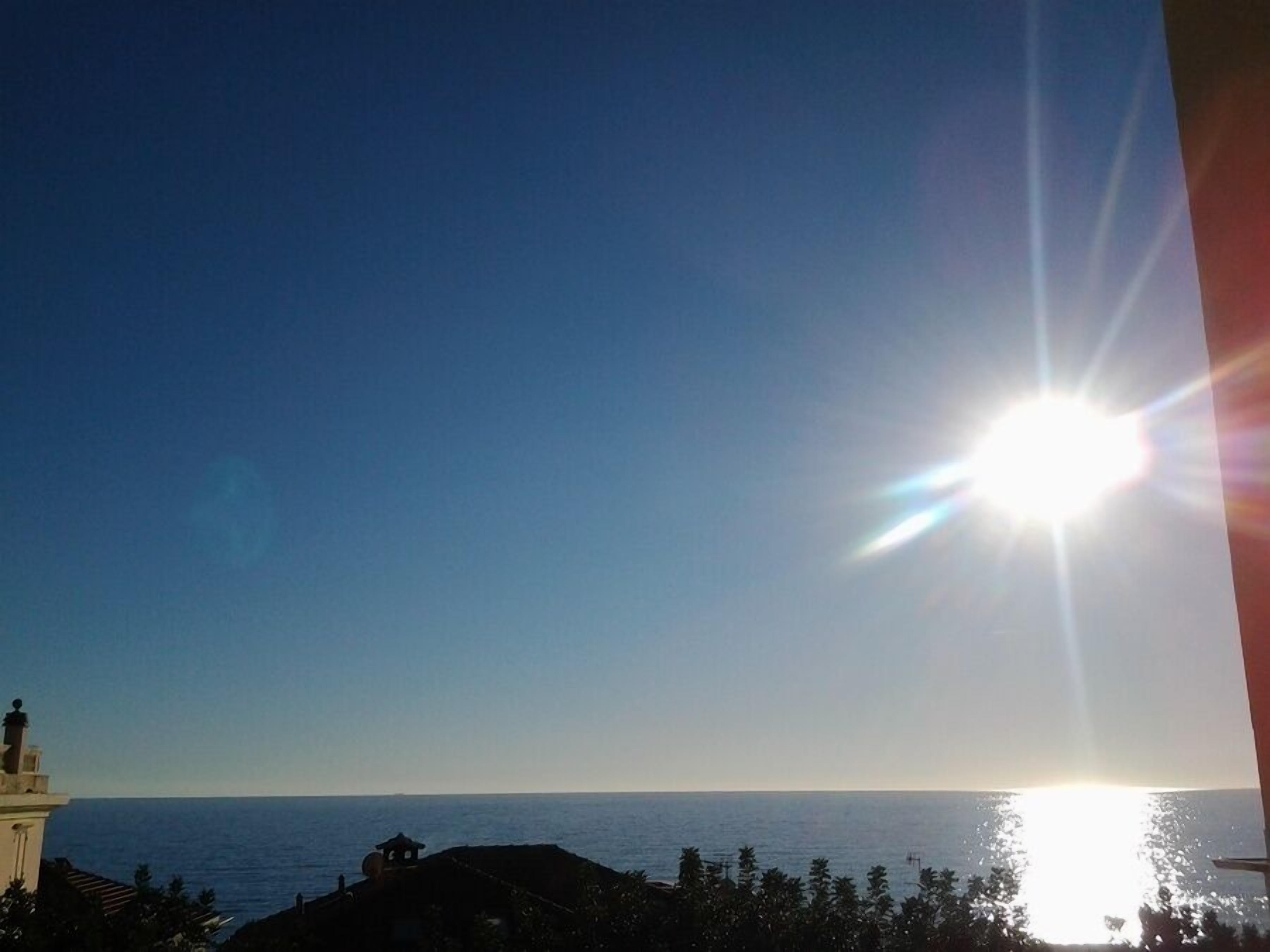 Eine Küstenansicht mit blauem Himmel, heller Sonne und weiter Ferne.