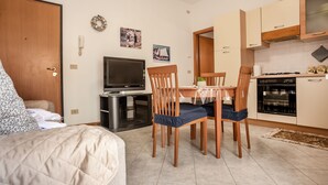 A compact living space with a bed, a dining table with chairs, a TV, a kitchen area with cabinets and appliances, and a small rug on the floor. - Residence Cava Zuccherina (Jesolo)