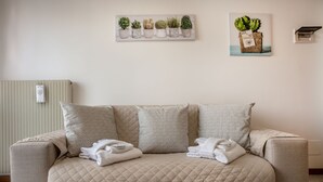 A beige quilted sofa with folded towels, a radiator, and a wall-mounted plant display. - Residence Cava Zuccherina (Jesolo)
