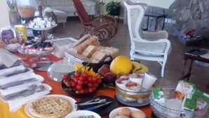 Mesa de comedor dispuesta con diversos alimentos y cubiertos, rodeada de sillas y una pared de piedra al fondo.