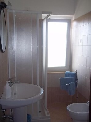 Un baño con ducha, lavabo, bidé y ventana que proporciona luz natural.