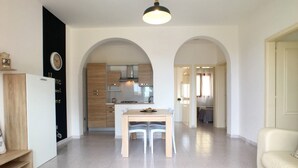 A modern kitchen with a dining area, featuring a central island, white chairs, and a light fixture above the table. - Villetta Gardenia (Morciano di Leuca)