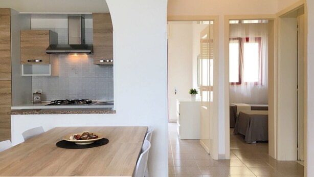 A modern kitchen with a built-in stove, white cabinets, and a dining area with a table and chairs. - Villetta Gardenia (Morciano di Leuca)
