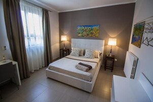 Habitación de hotel con cama, dos lámparas de noche, un cuadro en la pared y un radiador.