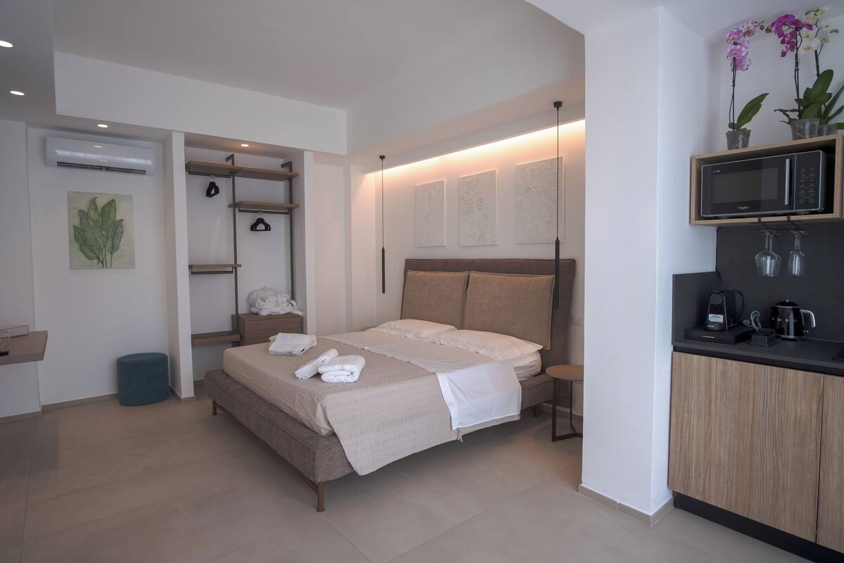 Un dormitorio moderno con cama, mesitas de noche, armario empotrado, un pequeño rincón de descanso y kitchenette.