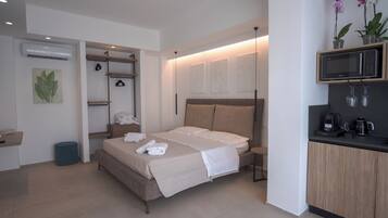 Une chambre moderne comprenant un lit, des tables de chevet, une armoire intégrée, un petit coin salon et une kitchenette.