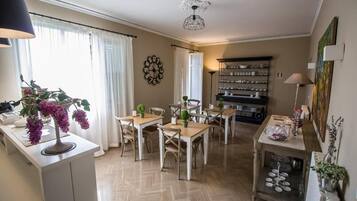 Comedor con suelo de espiga, mobiliario blanco y una mesa central con sillas. Cuenta con una zona de cocina con estantes y un radiador.