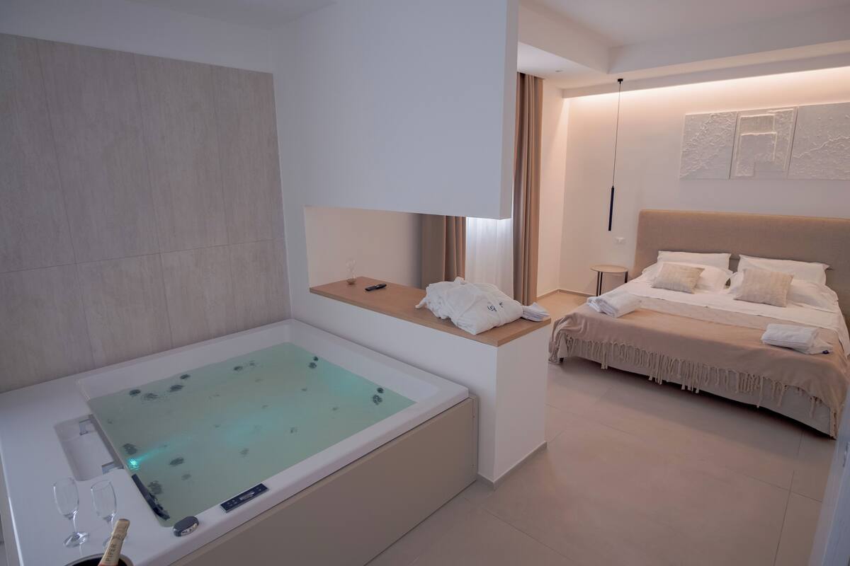Una habitación de hotel moderna con una bañera, una cama y una pequeña mesa con toallas.