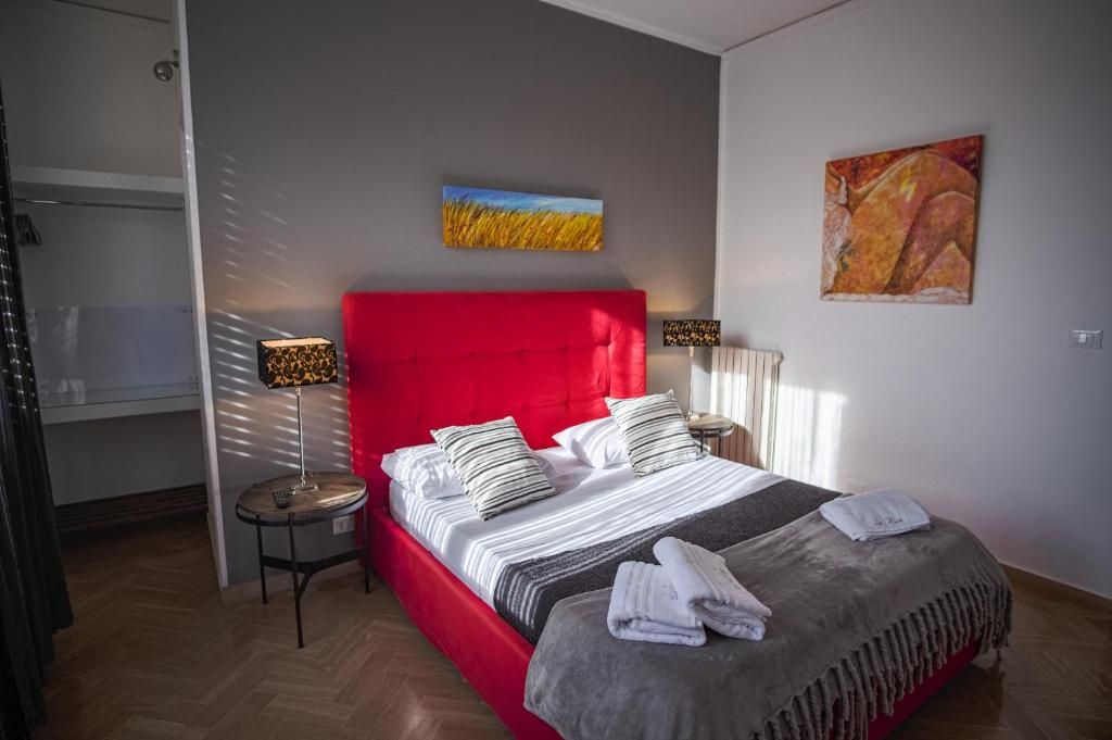 A bedroom with a red headboard, a bed with striped bedding, two bedside lamps, and artwork on the walls.
