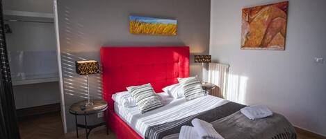 A bedroom with a red headboard, a bed with striped bedding, two bedside lamps, and artwork on the walls.