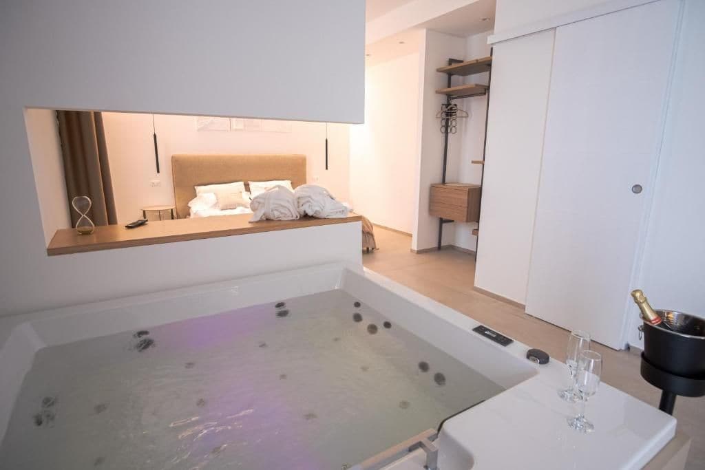 Une chambre d’hôtel moderne dotée d’une grande baignoire, d’un lit avec du linge de maison blanc, d’un minibar et d’un placard.