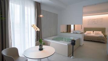 Una habitación de hotel moderna con un jacuzzi con paredes de vidrio, una cama con cabecera, una mesita de noche y una silla.