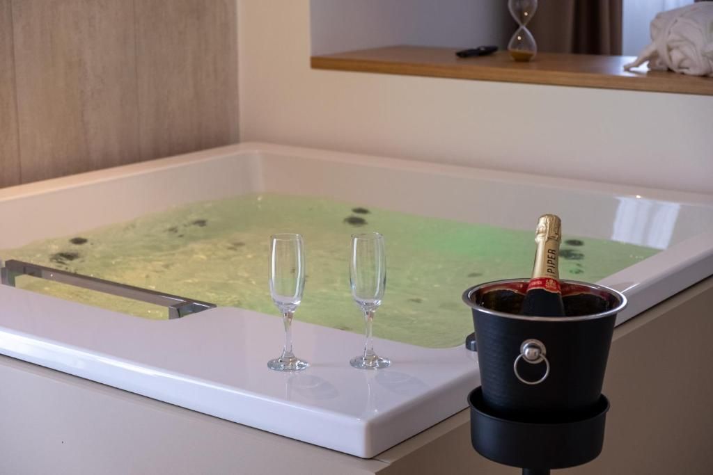 Una bañera con una fuente de agua verdosa, dos vasos vacíos y una botella de champán en un cubo.