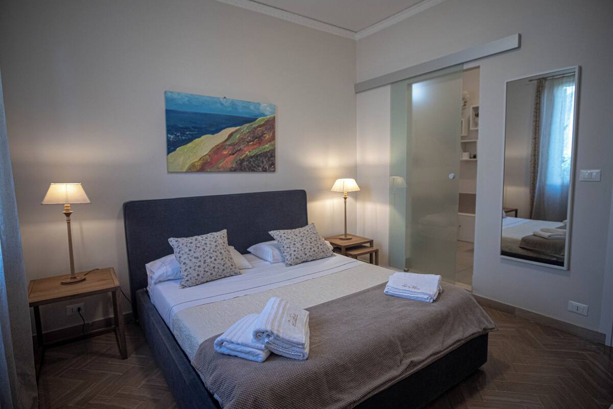 Una habitación de hotel con una cama grande, dos lámparas de noche, un cuadro en la pared y una puerta corredera que da al baño.