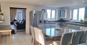A modern kitchen with a central island, a dining area with chairs, a refrigerator, and a view of the outdoors.