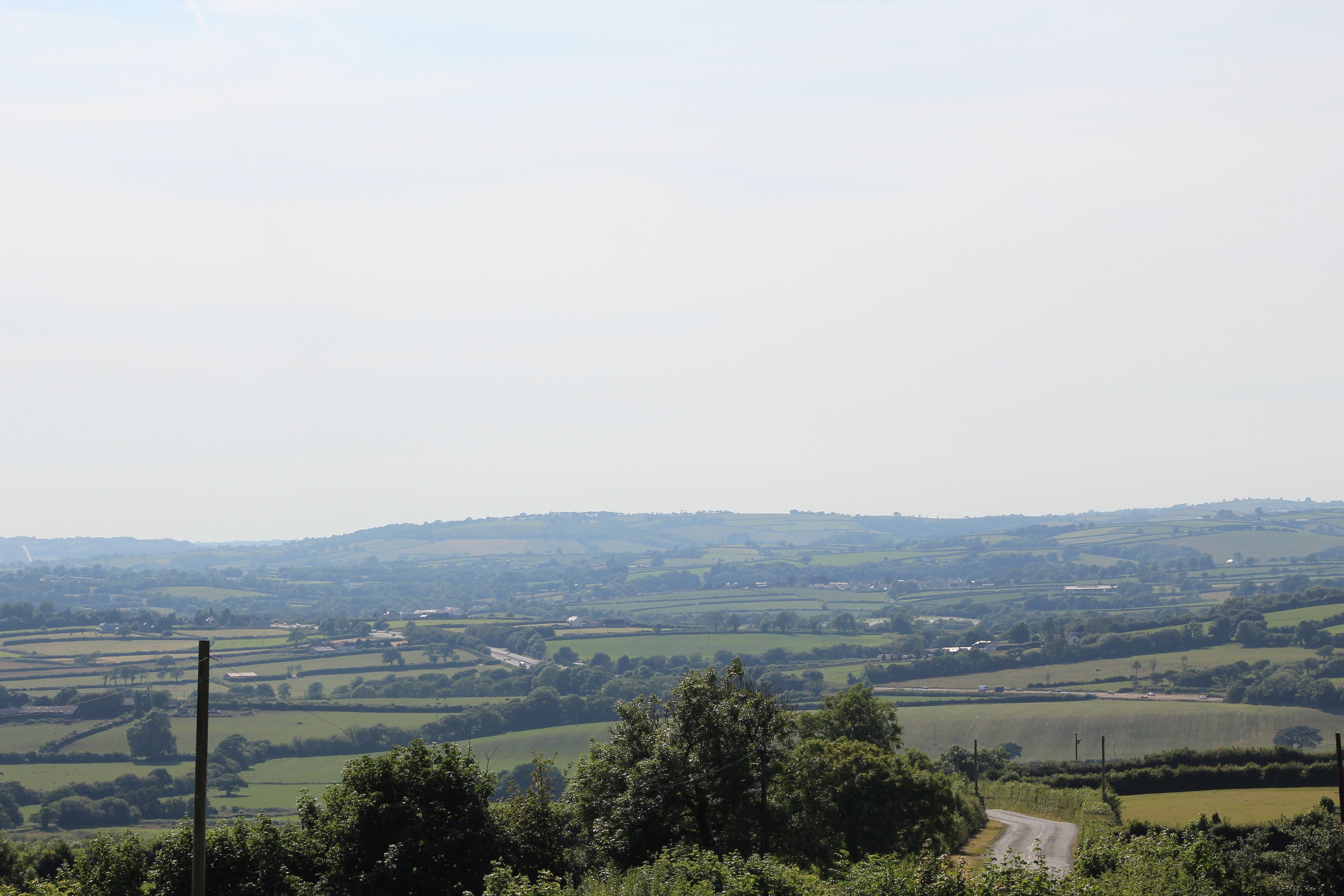 A rural landscape with rolling hills, a winding road, and scattered buildings.