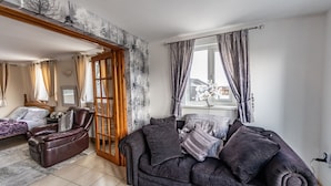 A living room with a dark brown leather sofa, a wooden door, and a view of a tree outside. - Bunny Meadows Farmhouse (Carmarthen)
