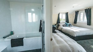 A hotel room with a glass shower enclosure, two beds with white bedding, and a window with curtains. - Bunny Meadows Farmhouse (Carmarthen)