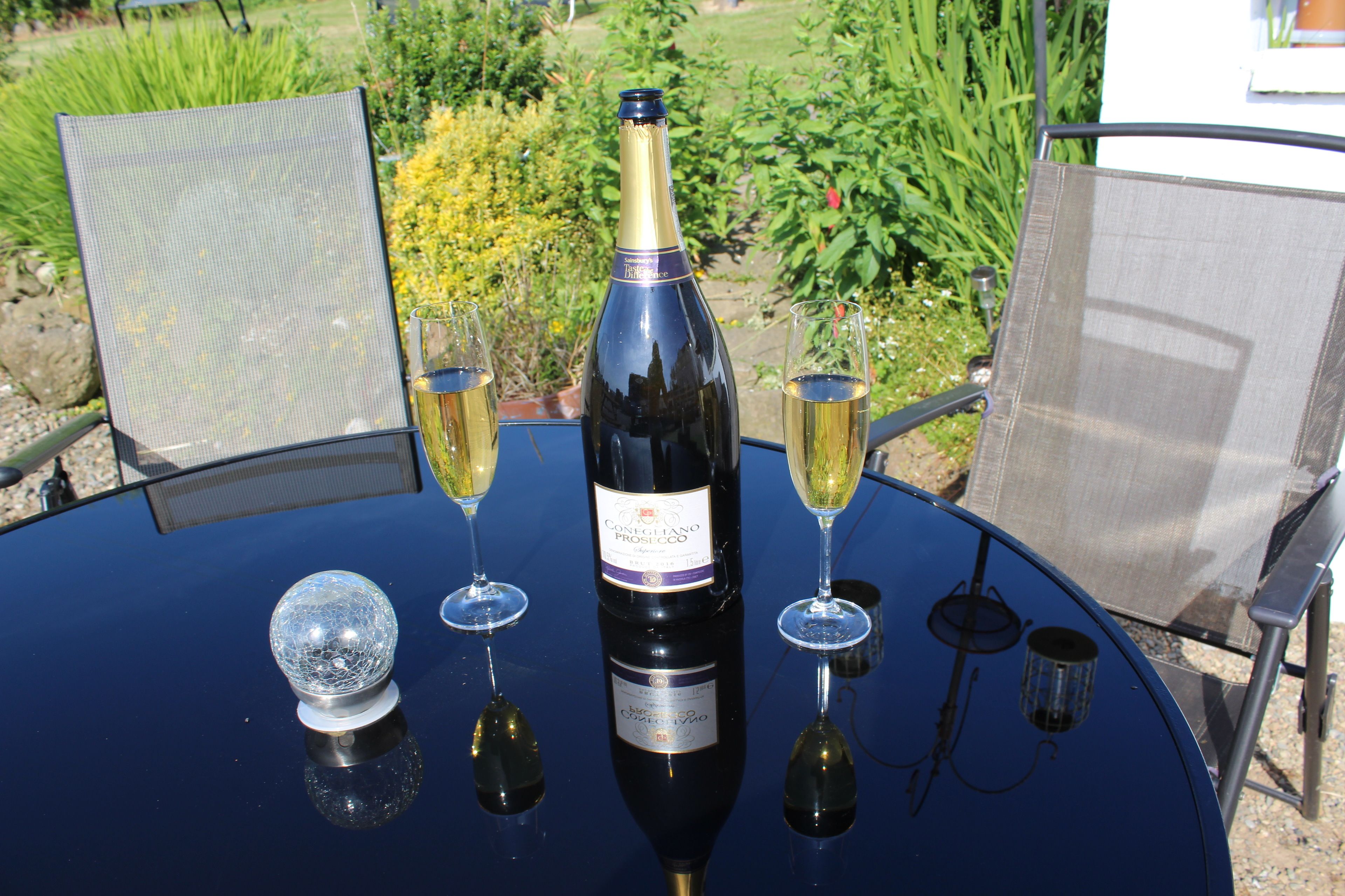 Ein Tisch mit einer Weinflasche, zwei Weingläsern und einem dekorativen Glas im Freien.