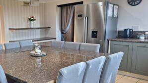A modern kitchen with a granite countertop, stainless steel appliances, and a dining area with a marble table and grey upholstered chairs. - Bunny Meadows Farmhouse (Carmarthen)