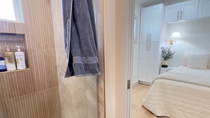 Ein modernes Badezimmer mit Dusche, einem Handtuch an der Wand und einem Ablagefach mit Pflegeprodukten.