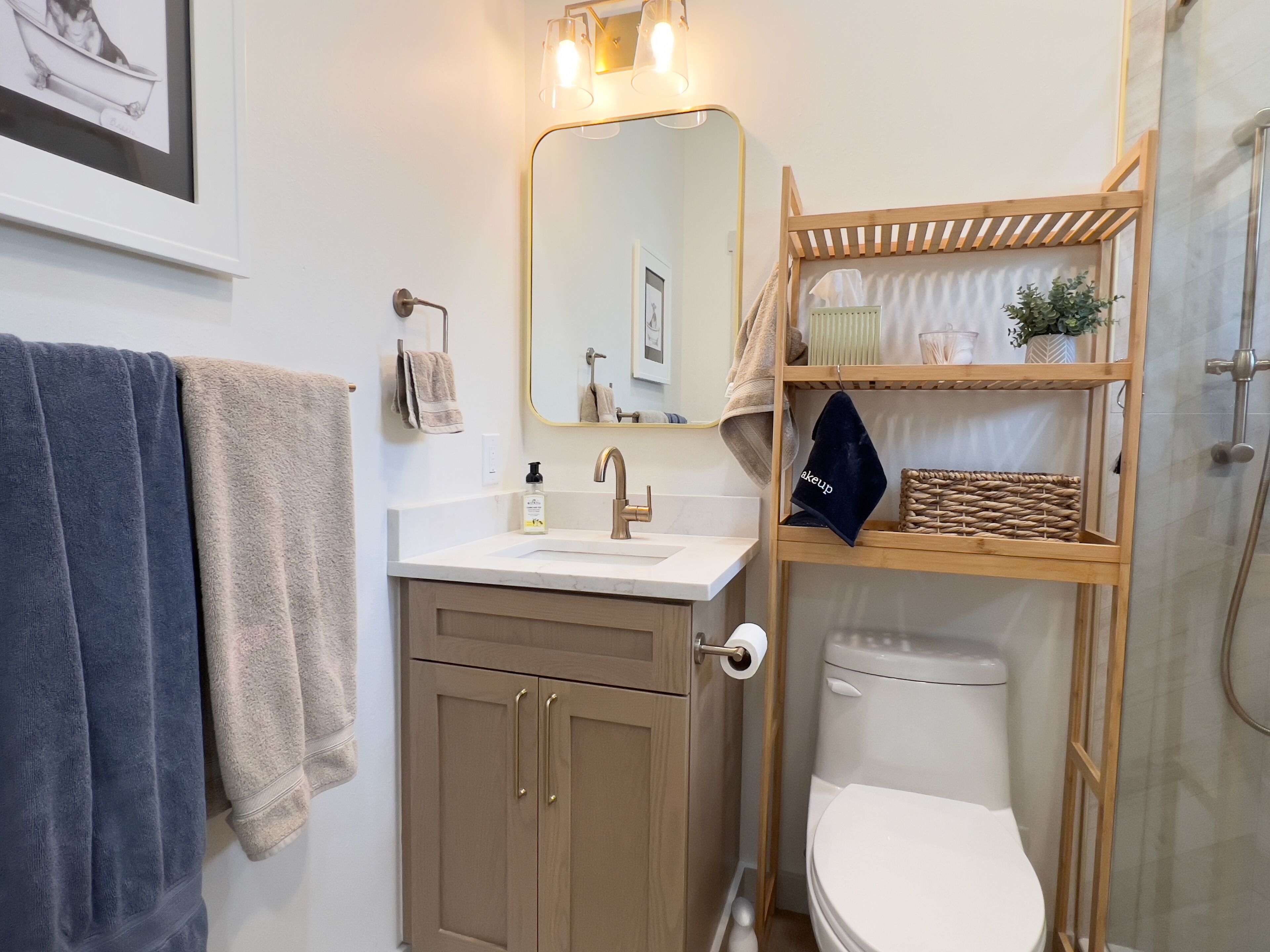 A bathroom with a sink, mirror, toilet, and a wooden shelf with toiletries.